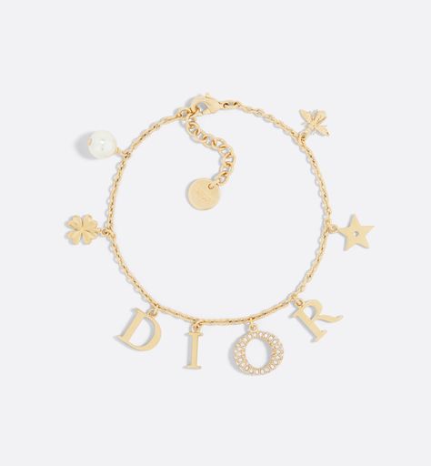 The Dio(r)evolution bracelet is a creation with a modern aesthetic. The Dior letters are suspended from a gold-finish metal chain, while the pavé of silver-tone crystals adorning the letter O adds a luminous touch. The design is embellished with a white resin pearl and signature Dior symbols, including stars, the clover and the bee. The sophisticated bracelet can be combined with other creations from the Dio(r)evolution line. Dior Charm Bracelet, Dior Armband, Dior Bracelet Gold, Bracelet Dior, Dior Jewellery, Dior Bracelet, Bracelets Luxury, Resin Pearl, Preppy Jewelry