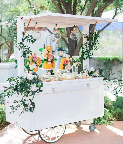 White food cart with green leaf decor and hanging bulb lights, yellow cakes and cupcakes {Photo: Andrew Jade / Cart: Ruze Cake House}