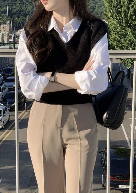 Achieve a timeless and polished look with this classic layered outfit featuring a black knit sweater vest over a crisp white button-down blouse. Paired with tailored beige trousers, casual and sophisticated. Whether for work or a coffee date, this look delivers effortless elegance. Accessorized with a sleek black leather bag and minimalist watch.  #LayeredLook #ClassicOutfit #BusinessCasual #MinimalistFashion #EffortlessChic #OOTD #styleguide Sweater Vest Formal Outfit, T Shirt With Jeans Outfits, Korean Classy Outfits, Aesthetic Lawyer, Neat Casual Outfits, Lawyer Fashion, Casual Work Outfits Women, Casual College Outfits, Chic Aesthetic