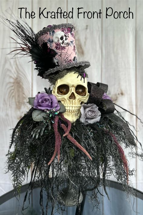 Add a touch of gothic elegance to your Halloween decor with this stunning skull centerpiece. This unique piece features a realistic skull adorned with a whimsical top hat, decorated with skulls, flowers, and a spider web design. The hat is accented with black feathers and lace, adding a sophisticated touch to the spooky aesthetic. The skull is nestled among an arrangement of faux purple and grey roses, eerie black foliage, and glittering accents, creating a hauntingly beautiful display. Perfect for your Halloween party, haunted house, or as a year-round statement piece for lovers of all things macabre. Scary Halloween Centerpiece Ideas, Sophisticated Halloween Decor, Halloween Eat, Mesa Halloween, Samhain Decorations, Skull Centerpiece, Tricky Tray, Halloween Centerpieces, Halloween Candlesticks