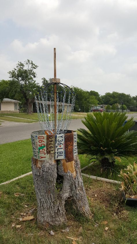 Homemade disc golf basket . Made of a old stump,hanging plant basket,   and old license plates. Diy Disc Golf Basket, House Playground, Cabin Landscaping, Hanging Plant Basket, Disk Golf, Disc Golf Basket, Disc Golf Baskets, Old License Plates, Disc Golf Courses