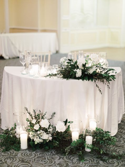 Ballroom sweetheart table with white linens and chiavari chairs and ivory and green centerpieces. Roses, wildflowers, hydrangea, and greenery. Floor arrangements and candles and repurposed ceremony centerpieces on acrylic risers. Hotel Del Wedding reception by Cavin Elizabeth Hydrangea Floor Arrangement, White And Green Sweetheart Table Flowers, Round Sweetheart Table Wedding, Sweetheart Table Greenery, Sweetheart Table Candles, Ceremony Centerpieces, Floor Arrangements, Hotel Del Coronado Wedding, Main Table Wedding