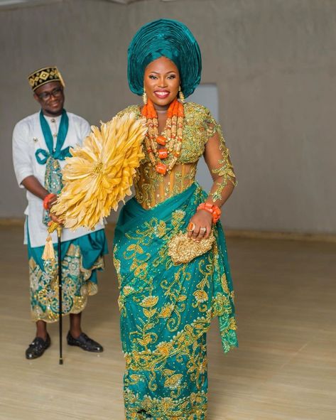 A picture showing an African man and woman wearing an Igbo wedding attire. The woman wears an Igbo wedding blouse and wrapper while holding a golden purse and a feathered traditional fan Igbo Blouse Styles, Igbo Blouse Styles For Wrapper, Blouse Styles For Wrapper, Igbo Traditional Attire, George Styles, Igbo Blouse, Nigeria Dress, Asoebi Lace Styles, Asoebi Lace