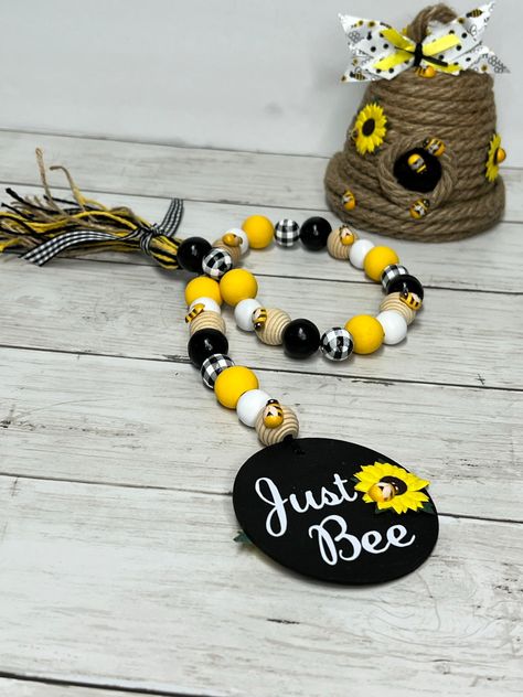 "Just Bee" honey hive and beaded garland set is buzzing with warm weather. Honey hive is made with large natural jute cord adorned with sunflowers and mini bees topped with black and white accented ribbon. Beaded garland has black, white, buffalo plaid, yellow and natural hive shaped beads complete with mini bees. Black round wood tag is double sided with "Just Bee", sunflowers and mini bees.Dimensions: Hive- 4.5 in x 4.5 in x 5 in H Garland- 27 in longReady to ship in 2-4 business days. **Tray Bee Garland Diy, Bee Crafts For Adults Diy, Bee Items, Bumble Bee Decorations, Bee Things, Bumble Bee Craft, Bee Rocks, Honey Hive, Bee Room