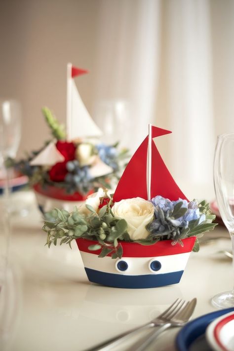 Nautical-themed centerpiece, perfect for baby shower centerpiece ideas, featuring a small red and white sailboat adorned with roses, blue flowers, and greenery. The boat is set on a table, surrounded by glassware and soft, natural lighting. Sailboat Centerpiece, Baby Shower Centerpiece Ideas, Sailor Hats, Striped Tablecloths, Sailor Hat, Budget Friendly Decor, Shower Centerpieces, Sea Inspired, Centerpiece Ideas