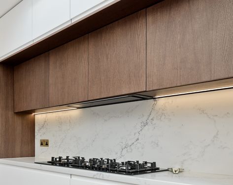 Downlighting over your prep area in your kitchen will make it easier for you to see when preparing a meal. It will also give the room a very contemporary and designed feel. To compliment this modern design, our client also chose to hide the extractor duct behind false cabinetry that matches real cabinets flanking the extractor hood. Concealed Hood Kitchen, Modern Extractor Hood Ideas, Kitchen Cabinet Hood, Modern Kitchen Extractor, Extractor Hood Ideas, Hide Kitchen, Kitchen Extractor Hood, Modern Kitchen Hood, New Kitchen Inspiration