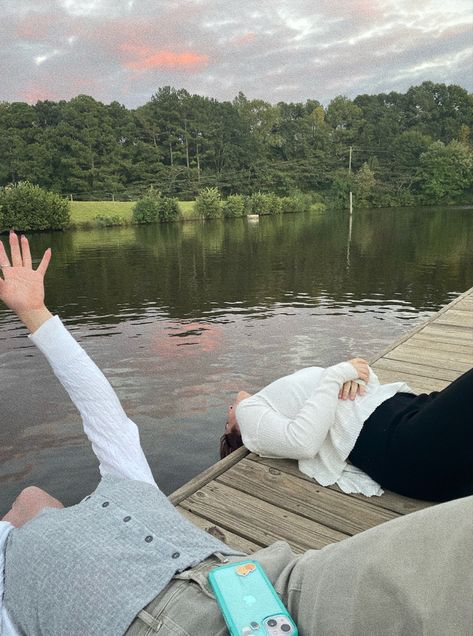 two girls are laying back down on a wooden dock, looking out into the lake behind them. the girl closest to the viewer has her hand raised towards the sky. behind the lake is a dyke and trees. the sunset is reflected in the lake. Lake Picnic, Sunset Friends, Lake Dock, Lake Summer, Double Dates, Dream Date, Summer Lake, Summer Getaway, Summer Sunset