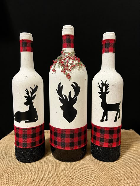 These wine bottles are some of my favorite items I have ever created. They give me a cozy winter cabin feel with your family under a red and black lumberjack blanket, hot chocolate & a wonderful Christmas movie! They are the perfect addition to all of your holiday decor and you can leave them up for the Winter as well! All reindeer are hand drawn and hand painted!  Left bottle: 12 in. Middle bottle: 13 in. Right bottle: 12 in. Beer Bottle Christmas Crafts, Creative Christmas Centerpieces, Wine Bottle Reindeer, Lumberjack Christmas Decor, Bottle Art For Christmas, Christmas Bottle Painting Ideas, Christmas Bottles Diy, Wine Bottle Santa, Christmas Painted Wine Bottles