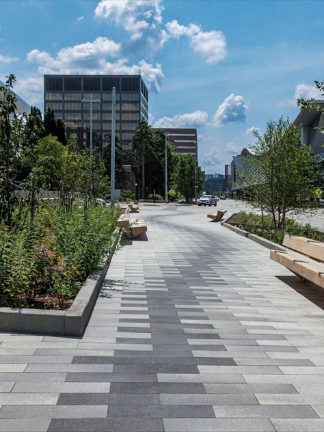 The final design suggests a boardwalk, using plank pavers through a riparian area which includes rain gardens and infiltration basins. The intent was to evoke movement through the space, while embracing the relationship to the Grand River which is only a block away, and providing areas of respite for downtown visitors and employees.
To achieve the desired paving pattern, three colors of 6” x 24” Promenade Plank Paver were used: Winter Marvel, French Grey and Midnight Sky in the Umbriano® finish. Paving Pattern Landscape, Diy Paving Ideas, Paver Block Design, Diy Paving, Pavers Walkway, Road Pavement, Paver Patterns, Pavement Design, Sidewalk Signs