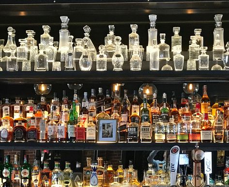 Assemblage of glass and crystal decanters  on the top shelf of a bar.  Here, the decanters (and the bottles of alcohol, below) are layered on three graduating levels per shelf. Home Bar Bottle Display, Bar Alcohol Display Design, Bar Glasses Display Shelves, Drink Shelf Ideas, Liquor Wall Display Bar Ideas, Alchohol Display, Alcohol Shelf Ideas, Bar Alcohol Display, Bar Glasses Display