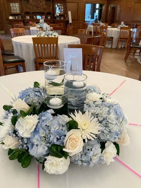 Difficulty: Medium     Wedding centerpiece   • Oasis foam ring  • 3 cylinder faces different heights  • 3 floating candles  • 5 blue hydrangeas   • 6 Fuji mums  • 8 cream roses  • 9 white carnations  • Pack of ruscus 5-6 stems   • Babies breath ￼2-3 stems  • Design master hydrangea blue ( for babies breath) Hydrangea Blue Centerpiece, Light Blue Wedding Flowers Centerpiece, Blue Carnation Centerpieces, Steel Blue Centerpieces Wedding, Blue And Cream Centerpieces, Fancy Centerpieces Wedding, Blue Wedding Centerpieces Round Table, Wedding Flower Arrangements Blue Table Centerpieces, Hydrangea Centerpiece Diy Wedding