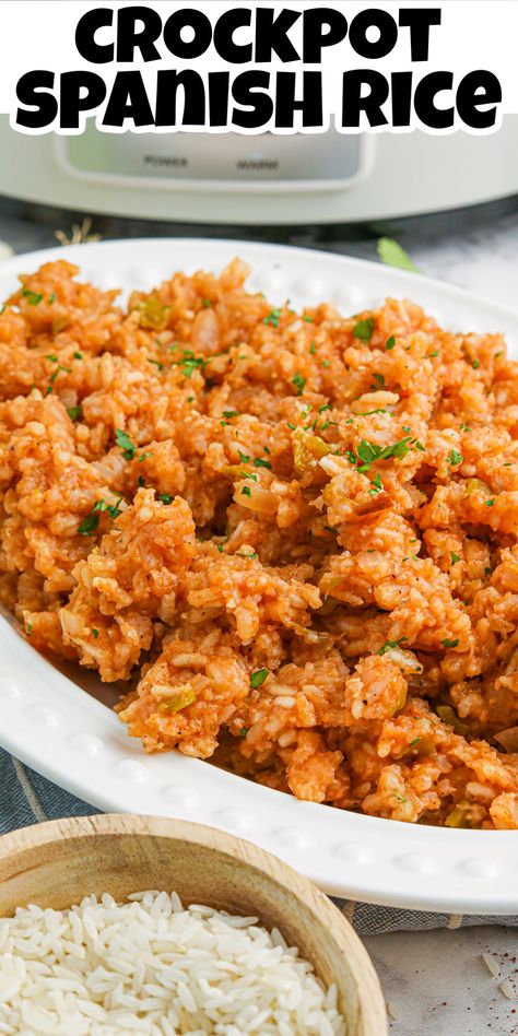 Overhead view of Crockpot Spanish Rice on a white platter in front of a crockpot with a wood bowl full of white rice. Spanish Rice Crockpot Recipes, Spanish Rice In Crock Pot, Crockpot Spanish Rice Easy, Crock Pot Mexican Rice Crockpot, Mexican Rice Crockpot, Crockpot Mexican Rice, Crock Pot Spanish Rice, Slow Cooker Spanish Rice, Crockpot Spanish Rice