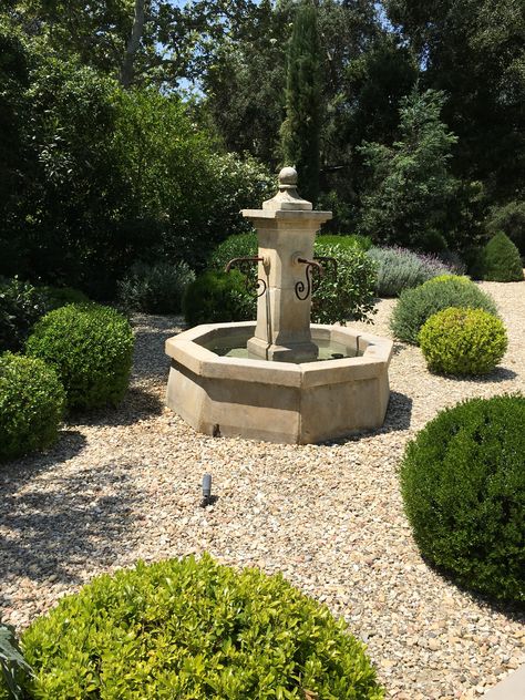 Our French Limestone fountains create the ideal centerpiece for your garden's design. This one shines in pea gravel and shrubs. Gravel Garden With Fountain, French Fountain Garden, Crushed Limestone Landscaping, European Backyard, Garden Corner Ideas, French Fountains, Courtyard Fountain, Limestone Fountain, Garden Fountains Outdoor