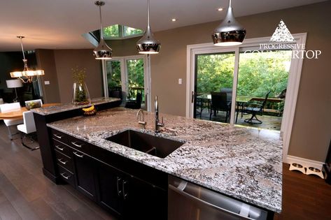 The natural beauty of Progressive Countertop’s Lennon Granite is complimented by the trees and greenery outside this kitchen’s large windows. Lennon Granite Countertops, Lennon Granite, Cambria Quartz Kitchen Countertops, Granite Kitchen Countertop, Granite Kitchen Countertops, Granite Kitchen Island, Colored Sinks, Family Room Remodel, Kitchens Design