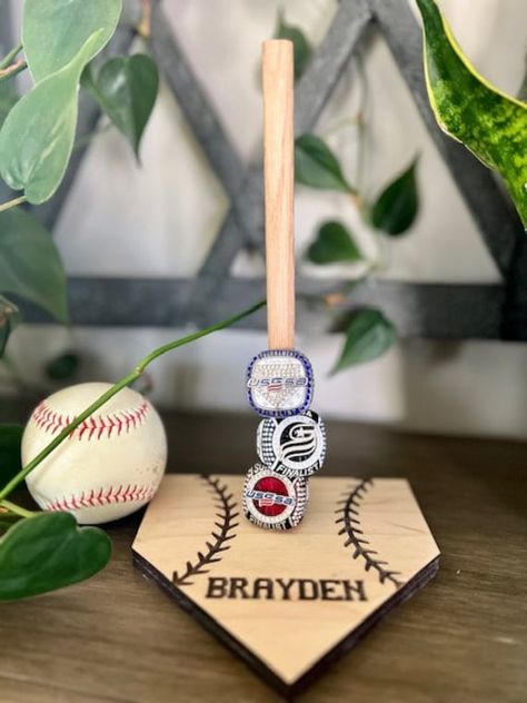 Looking for a way to display those baseball and softball tournament rings? Our wooden ring stand comes engraved with personalization of choice. Stand measures approximately 5.5 inches x 5.5 inches and stands approximately 8.75 inches in height. Base is made from maple ply and is laser cut and engraved. Display holds approximately 6-8 rings depending on size of individual rings. Choose between multiple stain colors or leave it unstained/natural! PERSONALIZATION: Each stand includes personalizatio Sports Ring Holder, Championship Ring Display, Baseball Ring Display, Baseball Player Gifts, Baseball Tournament Ideas, Softball Ring Display, Baseball Gifts For Players, Baseball Ring Holder, Baseball Themed Bedroom