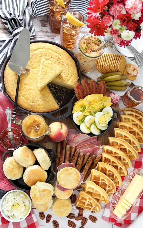 A pan of yellow cornbread, buttermilk biscuits, waffles, eggs, and other brunch fixings overflow a large serving board. Grits Waffles, Bourbon Syrup, Southern Brunch, Waffle Biscuits, Peach Bourbon, Brunch Board, Breakfast Spread, Southern Breakfast, Pimiento Cheese