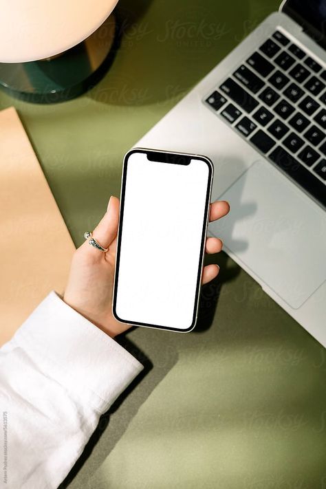 Woman With Cell Phone with a white screen at office. mockup phone. On the green table there is a pen, a notebook, a table lamp  and a laptop Phone On Table, White Screen, Phone Mockup, Green Table, A Notebook, A Table, Mockup, Cell Phone, Table Lamp