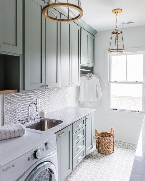 Gray green laundry room cabinets accented with brass knobs are fixed above a curved stainless steel sink paired with a polished nickel gooseneck faucet mounted in front of a white penny tile backsplash to a carrera marble countertop complementing gray green lower cabinets. Laundry Room Quotes, Laundry Room/mud Room, Green Laundry, Room Storage Diy, Dream Laundry Room, Mudroom Laundry Room, Farmhouse Laundry, Farmhouse Laundry Room, Laundry Room Cabinets