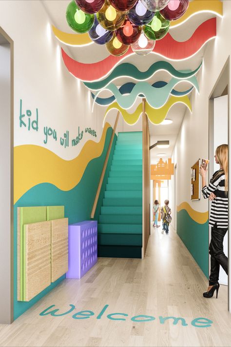 Statement wave effect ceiling and colourful ball lights with an Ombre effect staircase in turquoise. Kids you will make waves in a 3D font along the wall Kindergarten Design Interior, Daycare Entrance, School Wall Design, Kindergarten Interior Design, Kindergarten Entrance, School Wall Art Ideas, Childrens Ministry Decor, School Reception, Kindergarten Interior