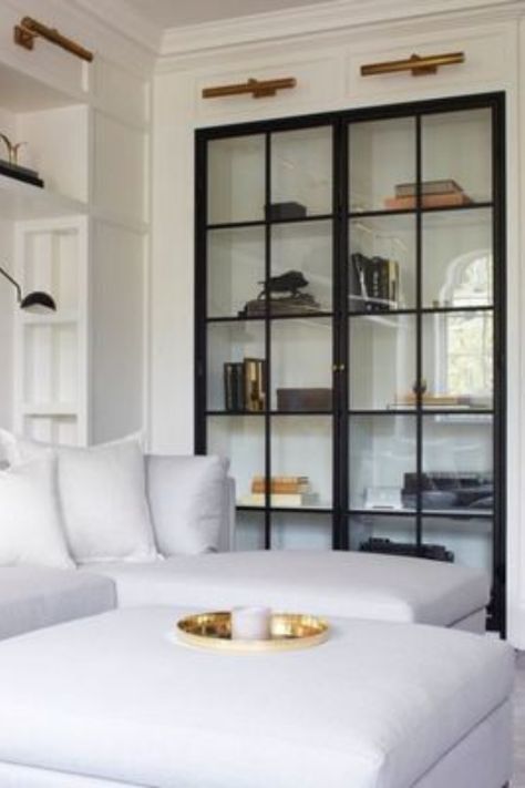 We greatly appreciate a beautiful built-in featuring glass doors! We also love the look of these black-frame glass doors and their contrast to this bright, white living area. Read our blog post for more built-in design inspiration. #interiordesign #interiordesigner #built-ins #built-in #shelves #glassdoors #whitesofa #sofa #shelfstyling #gallerylights #bookshelves Glass Shelves In Bathroom, Glass Shelves Decor, Glass Cabinet Doors, Glass Cabinet, A Living Room, Book Shelf, Cheap Home Decor, Built Ins, Home Decor Accessories