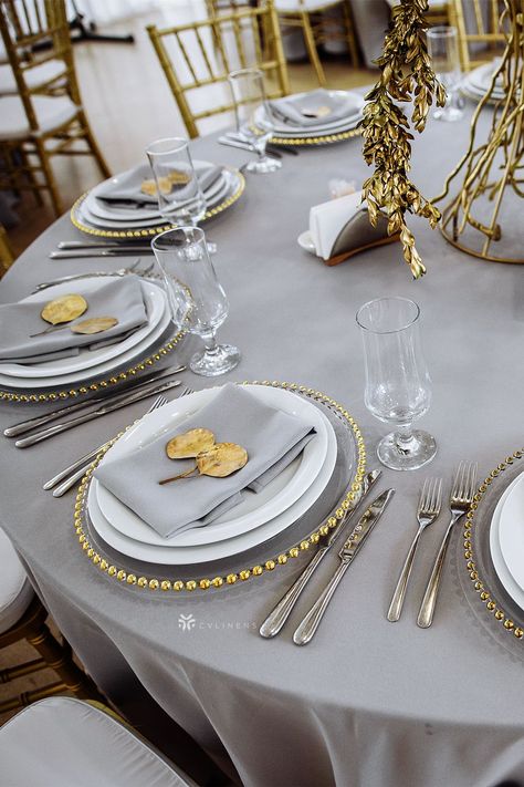 Gray polyester linens from CV Linens offer a simple yet sophisticated way to dress up your table. When paired with gray napkins, gold beaded charger plates and gold center pieces, you will create a classic base for an elegant tablescape. The subtle color is a perfect color to compliment other colors allowing you to decorate for any event theme. gray wedding colors, gray table setting wedding, gray table decor, gray wedding theme, silver gray wedding theme Sophisticated Table Settings, Napkins Table Settings, Charger Table Setting, Silver And Gold Table Decor, Silver Gold Wedding Theme, Gold And Silver Wedding Theme, Silver Gold Wedding, Napkins On Charger Plates, Silver And Gold Table Decorations