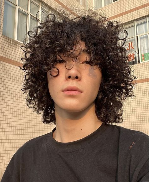 Asian boy with curly hair and a black top. The background is a checkered orange building with a few windows. Curly Hair Asian Guy, Asian Curly Hair Men, Asian With Curly Hair, Japanese Curly Hair, Jellyfish Haircut Men, Mixed Asian Men, Curly Hair Asian, Asian Curly Hair, Curly Asian Hair