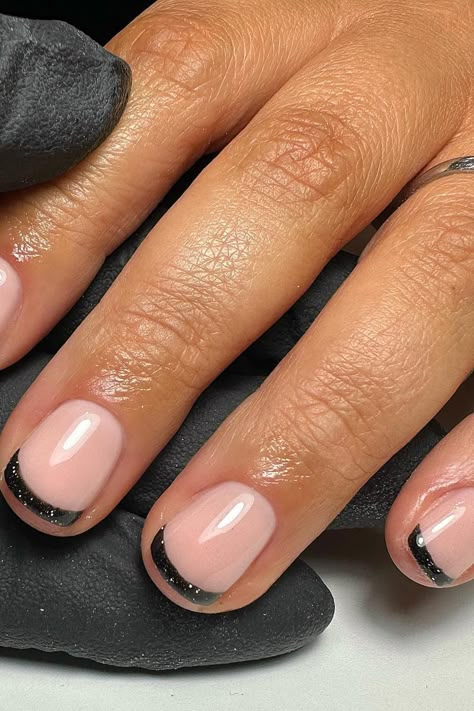 Elevate your nail game with these stunning glossy black glittery French tips on short squoval nails, blending timeless elegance with a contemporary edge. The soft pink base creates a delicate and natural aesthetic, while the bold black tip entices with a subtle sparkle, bringing a stylish modern twist to the classic French manicure! ✨ // Photo Credit: Instagram @kirstnailartist Dark Tipped Nails, Anc Ombre Nails, French Manicure With Black Line, Black Nails Sparkle Tips, Alternate French Manicure, Black Glittery Nails Short, Modern French Manicures, Black Nails Easy Design, Black Donut Glaze Nails