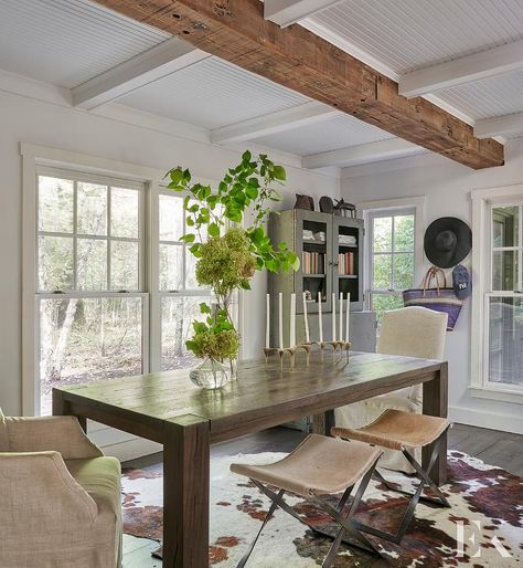 Cottage dining room featuring a dark brown wooden dining table joined with linen dining chairs and cowhide x stools. Cowhide Rug Dining, Cowhide Rug Dining Room, Brown Cowhide Rug, Bamboo Dining Chairs, French Dining Tables, Brown Dining Chairs, Cottage Dining Rooms, Brown Dining Table, Modern Farmhouse Dining Room