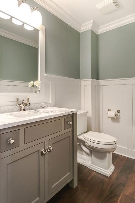 Tranquil bathroom features upper walls painted gray green and lower walls clad in board and batten lined with a creamy gray washstand topped with white marble under a white Parsons mirror illuminated by a three light downlight sconce. Bathroom Wainscoting Ideas, Bathroom Wainscoting, Wainscoting Height, Makeover Kamar Mandi, Tranquil Bathroom, Wainscoting Bathroom, White Wainscoting, Diy Wainscoting, Upstairs Bathrooms