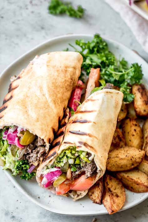 Beef shawarma sandwich rolled up in a pita bread and cut in half on a plate, alongside baked potato wedges and fresh parsley. Shwarma Beef, Recipes Wraps, Shawarma Sandwich, Baba Ganush, Beef Kebab, Kebab Wrap, Beef Shawarma, Arabisk Mad, Baked Potato Wedges