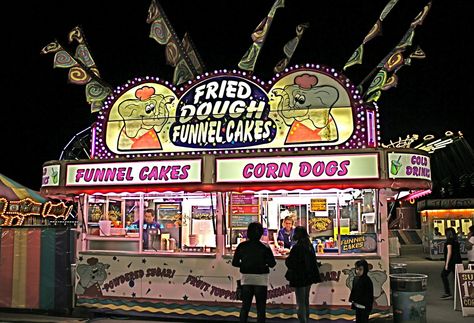 Concession stand at a nighttime carnival. Carnival At Night, Aesthetic Carnival, Senior Thesis, Pool Floaties, Roller Rink, Carnival Rides, Concession Stand, Funnel Cake, Corn Dogs