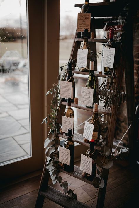 Wooden ladder seating chart finished with empty wine bottles and green foliage decor Unique Seating Chart Wedding Display, Wedding Sitting Charts, Wine Cork Seating Chart, Blanket Ladder Seating Chart, Bottle Seating Chart Wedding, Wine Bottle Table Plan, Wine Seating Chart, Wedding Wine Bottle Decor, Wine Seating Chart Wedding