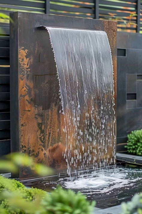 A rustic metal wall fountain with water gracefully flowing over a textured surface, surrounded by greenery in a stylish garden setting. Outdoor Patio Fountain Ideas, Water Features Backyard, Water Feature For Patio, Diy Outdoor Waterfall Fountain, Waterfall Water Feature, Metal Water Feature, Water Features In The Garden Fountain, Mini Fountain Garden, Water Feature Wall Outdoor