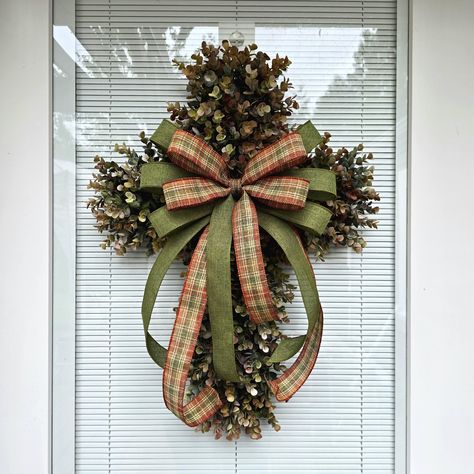 This beautiful handmade cross wreath is made with high-quality artificial eucalyptus foliage, which is densely packed to create a full and robust wreath. The wreath is designed with a wired ribbon bow placed in the center. The ribbon bow in the center is removable, and you can add ornamental adornments such as flowers, bows, and signage to the eucalyptus wreath base to suit your needs and the season you are decorating for. 📿MEASUREMENTS: The completed measurements for this wreath are approximately 25" H x 19" W x 4" D. It is a perfect size for front doors, entryways, and any indoor or outdoor wall decor. This wreath is assembled on a 20" x 13" plastic board constructed from 100% recycled plastic. It is weather, fade, and rust-resistant, making it durable and perfect for outdoor use. Due t Wreaths For Office Door, Cross Door Wreath, Cross Wreaths For Front Door, Dollar Tree Cross Wreath Ideas, Church Entryway Decor, Christmas Cross Wreath, Church Wreaths, Burlap Cross Wreath, Cross Wreaths