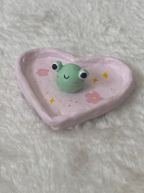 Handmade clay jewelry dish/trinket of a heart with a frog in the middle of a heart; beautiful little dish to be used to store jewelry or simply as decor! Made with stone air dry clay, acrylic paints, and sealed with glaze. Please message me for customs! Made by Jess & made with ♡. Clay Frog Dish, Jewelry Holders Clay, Air Dry Jewelry Dish, Frog Trinket Dish, Cute Clay Bowls, Air Dry Trinket Dish, Air Dry Jewelry, Airdrying Clay Projects, Baked Clay Crafts