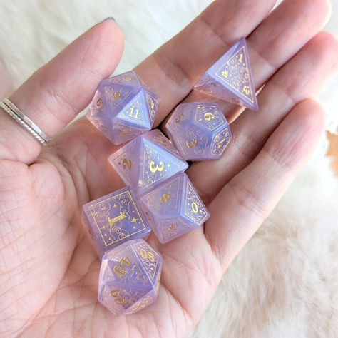 Introducing our latest addition to the collection - a stunning new dice set design featuring intricate swirling clouds, a crescent moon, and stars, all contained within a geometric border. These beautiful purple opalite dice are adorned with gold engravings that add a touch of elegance and magic to each die. We underst Purple Dnd Dice, Dice Sets Dnd, D&d Setup, D&d Gifts, Cute Dnd Dice, Hobby Ideas Aesthetic, Dnd Dice Aesthetic, Mystery Aesthetic, Dice Ideas