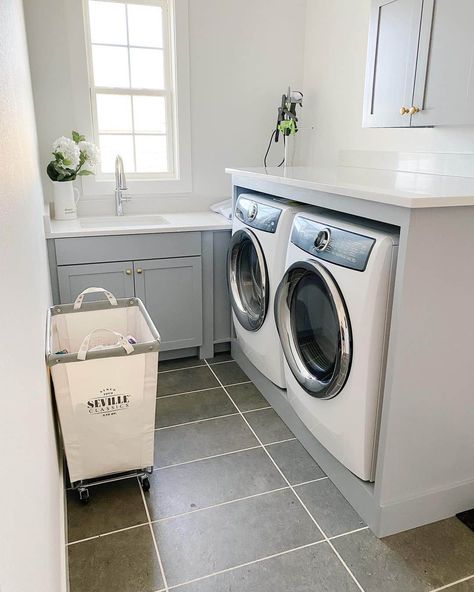 These light gray laundry room cabinets are topped by a white countertop. The room is finished with gray rectangular floor tiles. Enclose your washer and dryer under a gray counter with a white countertop to create a nifty folding station in a small space. Counter On Top Of Washer And Dryer, Small Laundry Space, Grey Laundry Rooms, Gray Counter, Laundry Cabinets, Laundry Room Layouts, Laundry Room Cabinets, Small Laundry, Small Laundry Room