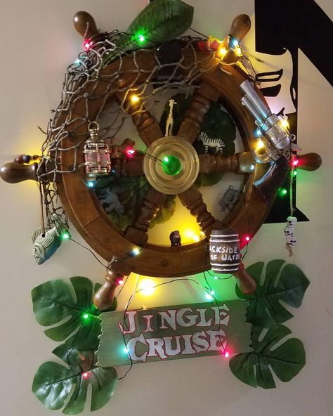 A Christmas wreath made to represent Disneyland’s Jungle Cruise attraction, centered around a ship steering wheel, decorated with Christmas lights and jungle themed items like nets, barrels, and a pistol. Faux exotic greenery compliment the look which is complete with its final touch of a “jingle cruise” sign hanging from the bottom. Jungle Cruise Vbs Decorations, Jungle Cruise Decorations, Adventureland Aesthetic, Jumanji Homecoming Float, Jungle Cruise Birthday Party, Jungle Cruise Vbs, Disney Jungle Cruise Nursery, Jungle Cruise Decor, Disney Jungle Cruise Decor