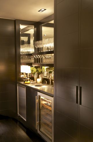 Sleek modern wet bar with espresso cabinetry. The bar area is flanked by cabinets, it features a mirrored interior and espresso stained floating shelves for glasses. A built-in mini fridge and glass fronted wine fridge sit below the counter. A black countertop is paired with an undermount bar sink and polished nickel faucet. Paul Davis - New York Modern Wet Bar, Modern Bar Cabinet, Undermount Bar Sink, Espresso Cabinets, Home Bar Areas, Home Bar Designs, Mini Bars, Bar Interior, Basement Bar