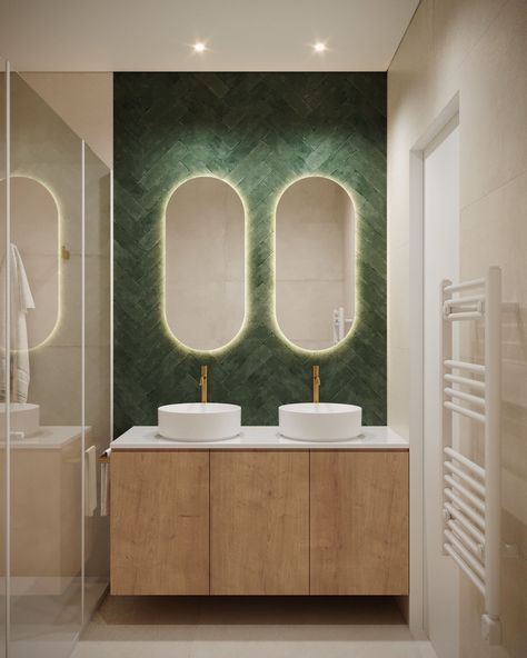 Modern and elegant bathroom vanity area with a unique and striking design. The focal point is the deep green herringbone-patterned wall, which adds texture and richness to the space. Two oval mirrors are mounted above the double sinks, each backlit with soft, warm lighting that highlights their shape and creates a cozy atmosphere. Bathroom Vanity Area, Elegant Bathroom Vanity, Oval Mirrors, Green Tiles, Double Sinks, Patterned Wall, Vanity Area, Warm Lighting, Green Tile