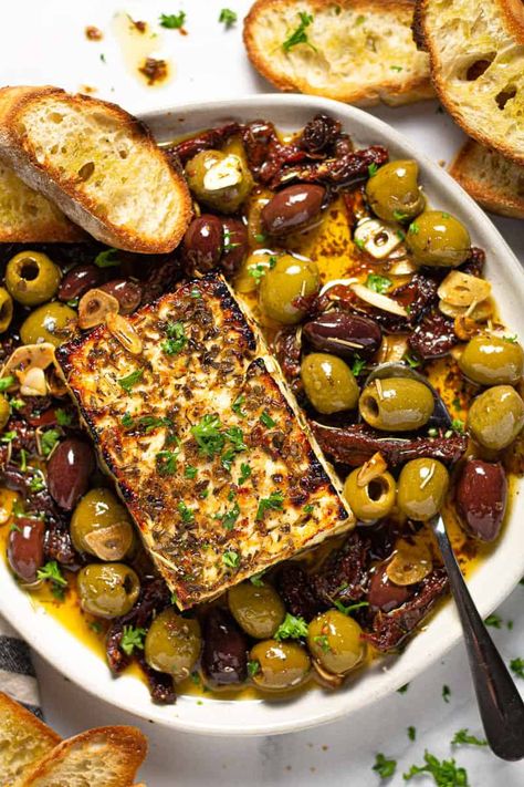 This Baked Feta Appetizer comes together in just minutes with only a handful of ingredients - olives, sun-dried tomatoes, fresh garlic, olive oil, and herbs. Bake it all together with a block of feta cheese until it's warm and creamy then serve with crispy crostini! Olives Appetizer, Crispy Crostini, Feta Appetizer, Mini Aperitivos, Baked Feta Recipe, Roasted Olives, Feta Cheese Recipes, Baked Feta, Feta Recipes