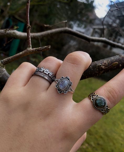 A person’s hand with multiple silver crystal rings on it. Silver Jewelry Aesthetic Rings Grunge, Black Jewellery Aesthetic, Fairygrunge Rings, Earthy Rings Aesthetic, Crystal Rings Silver, Dark Silver Rings, Layered Rings Silver Grunge, Dark Fairycore Jewelry, Rings Goblincore