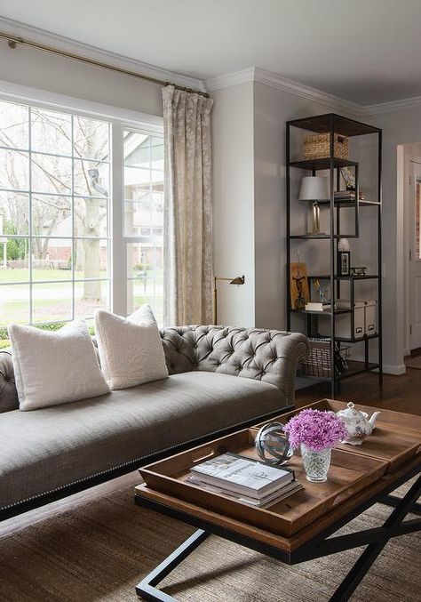 A gray tufted sofa accented with white pillows sits on a jute rug in front of windows dressed in gray floral curtains. Sofa In Front Of Window, Couch In Front Of Window, Grey Tufted Sofa, Light Gray Couch, Living Room Redesign, Jute Rug Living Room, Organic Living Room, Transitional Living Rooms, Tufted Sofa