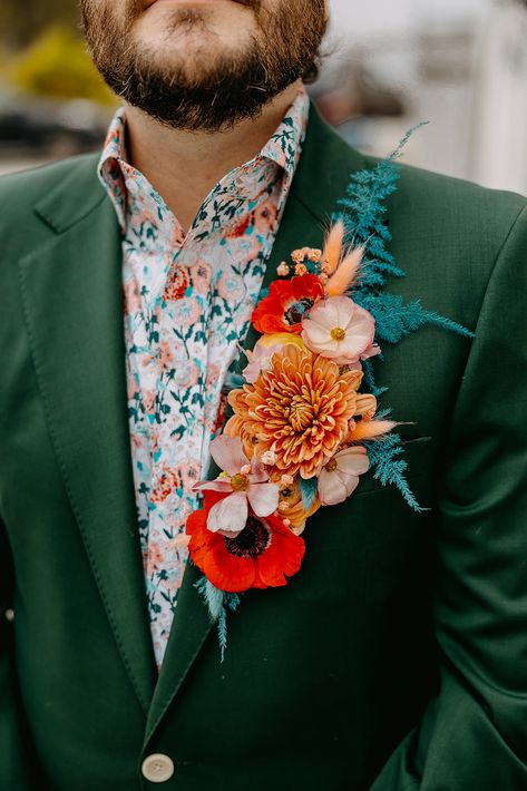 Daniel was equally stylish in a deep green suit and a floral shirt that managed to pull in every other color from their wedding design. But, by far our favorite part of his look–the colorful boutonnière that stretched the length of his lapel! Floral Lapel Groom, Jewel Tone Groom, Nontraditional Groom Attire, 70s Groom Suit, Suit With Floral Shirt, Deep Green Suit, Unique Groom Attire, Hobo Wedding, Groom Suit Ideas