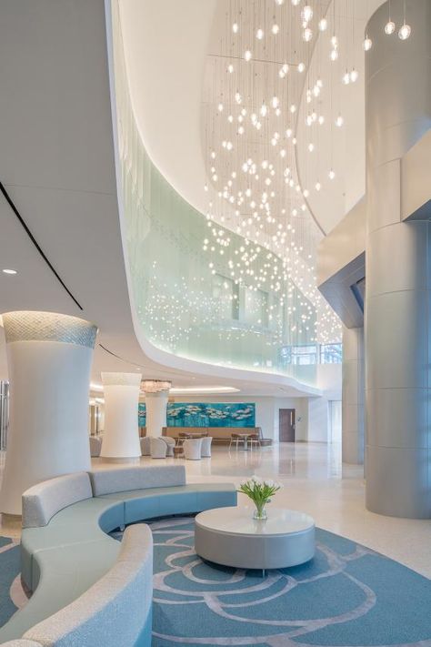 A water theme is incorporated into the interior materials, lighting, and art selection, as shown in the double-height main lobby, to symbolize purity, healing, and fertility. Credit: Michael Stavaridis Photography Interior Design Competition, Lazy River Pool, Healthcare Interior Design, International Interior Design, Cool Office Space, Office Decor Professional, Loft Interior, Hospital Interior, Lobby Interior