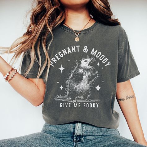 Join the 'Feral and Pregnant Club' with this playful and quirky pregnancy reveal shirt! Perfect for soon-to-be moms who embrace the chaos, this opossum-themed tee makes a fun announcement to family or a unique gift for first-time moms. Whether you're wild at heart or just navigating pregnancy with a feral spirit, this shirt is a must-have for your maternity wardrobe! Product Details: 📏 Sizes offered: Check out the drop-down menu for all our sizes 🎨 Colors: Explore the drop-down menu and photos for color options 🌟 Material: 100% garment-dyed soft ring-spun pre-shrunk cotton fabric--super comfy 👕 Style: Short sleeve unisex t-shirt--perfect for everyone 🧼 Care: Machine wash cold, delicate inside out with like colors. Tumble dry low or hang to dry, 🖨️ Graphic: Professionally direct to ga