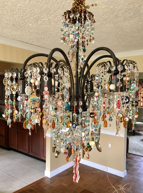 Upcycled chandelier with found objects, shells, watches, fishing lures, crystals, stones, buttons, beads, recycled glass beads, vintage jewelry, pins, coins,  and resistors, and keys. Finished with a fused glass piece of bacon. Fishing Lure Chandelier, Recycled Chandelier Ideas, Chandelier Glass Upcycle, Upcycled Chandelier Ideas, Upcycle Chandelier, Chandelier Upcycle, Glass Bead Chandelier, Upcycled Chandelier, Cool Chandeliers