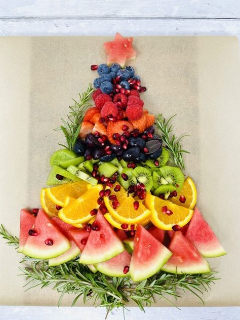 fruit platter being made in shape of Christmas tree - layer of rosemary sprigs, followed by watermelon, sliced oranges, sliced kiwis, sliced grapes, sliced strawberries, raspberries and blueberries with a star on the top cut from a slice of watermelon Christmas Fruit Snacks, Christmas Fruit Platter, Festive Fruit Platter, Christmas Platters, Cousins Christmas, Christmas Fruit Salad, Camp Christmas, Christmas Veggie Tray, Fruit Board