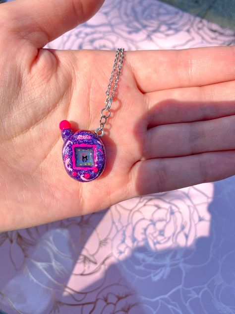 Adorable handmade tamagotchi necklace. Can be customized with any color and design! Screen glows in the dark Clay Tamagotchi, Clay Tomagatchi, Tamagotchi Mimitchi, Tamagotchi Necklace, Purple Tamagotchi, Tamagotchi Charm, Tamagotchi Clay Charm, Giga Pet, Tamagotchi Acrylic Keychain