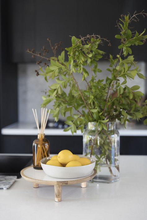 Vignettes or styled arrangements add interest to surface areas of your home. They are also a great way to display your favourite items! You can put them on your coffee tables, sideboards, kitchen benches, beside table, shelves and so much more! We give you the best tips and tricks on how to create and style a vignette in your space. Kitchen vigentte styling with stylised tray, aroma diffuser, bowl of fruits, lemons, large vase, foraged branches. Click the pin to see more vignette inspo and tips! Kitchen Bench Fruit Bowl, Fruit Bowl Decor Centerpieces, Fruit Bowl On Island, Bowl Of Lemons Decor, Farmhouse Fruit Bowl, Lemon Bowl Decor, Wooden Risers Display Kitchen, How To Display Fruit On Counter, Fruit Display Ideas Kitchen